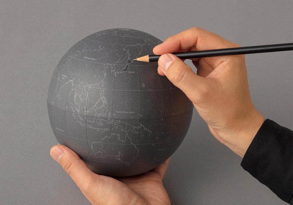 A person drawing on a gray PLOTTER Paper globe.