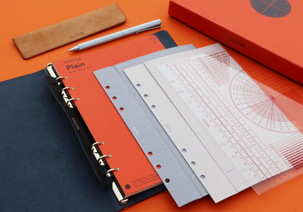 A PLOTTER Leather Binder opens to a blank page with different stationery accessories around it.