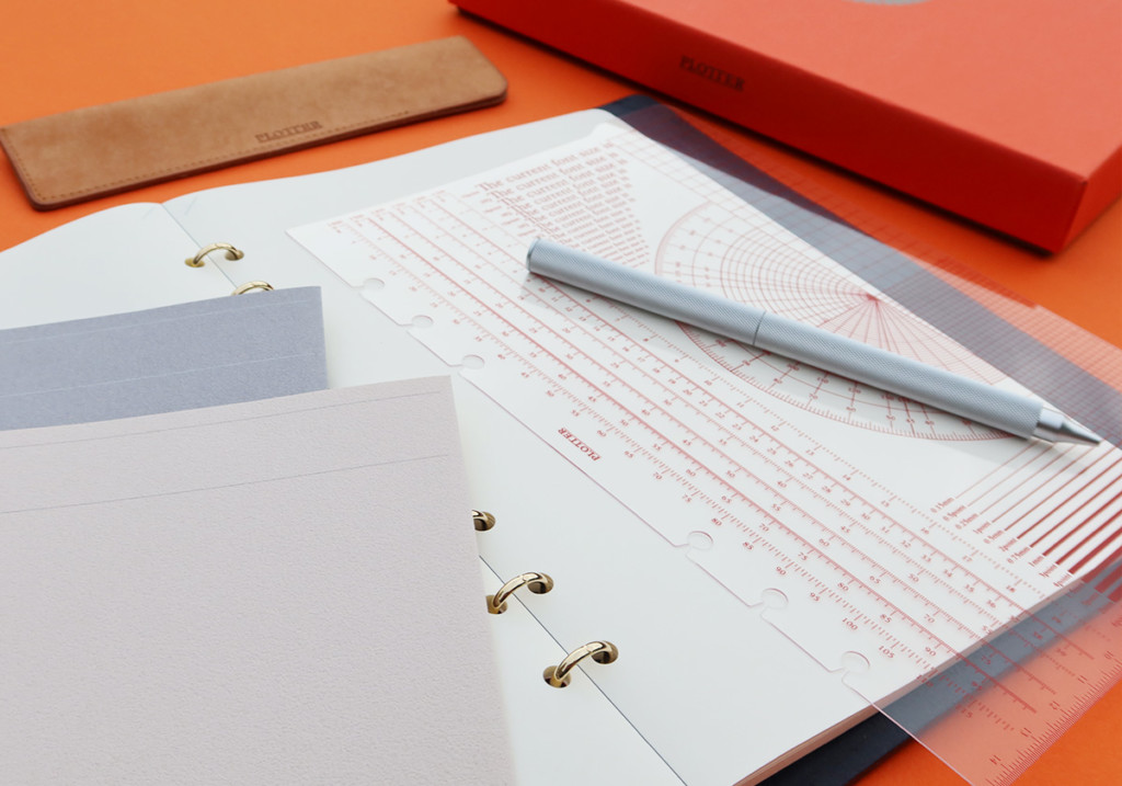 A PLOTTER Leather Binder opens to a blank page with different stationery accessories around it.