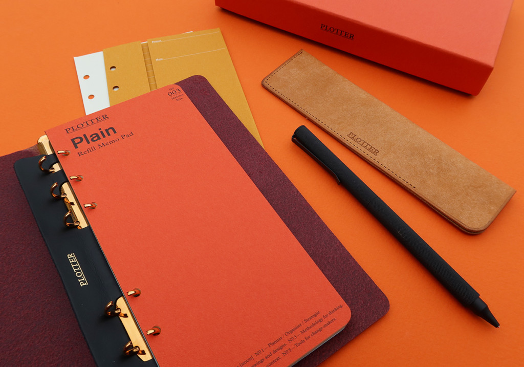 A PLOTTER Leather Binder opens to a blank page with different stationery accessories around it.