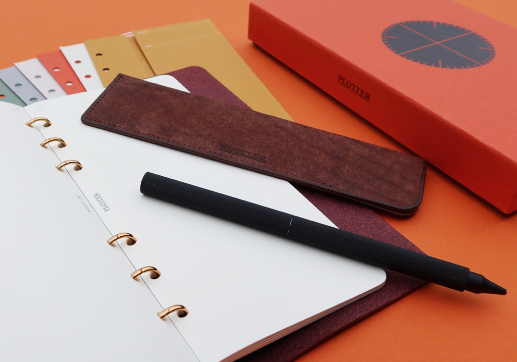 A PLOTTER Leather Binder opens to a blank page with different stationery accessories around it.