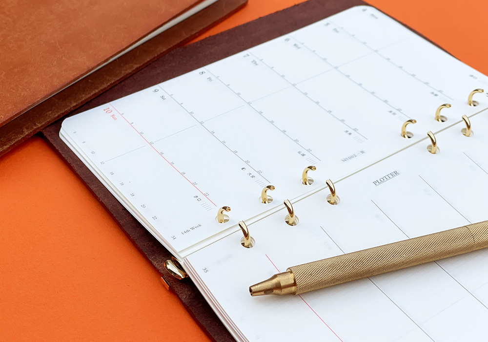 A PLOTTER Leather Binder opens to a weekly calendar.