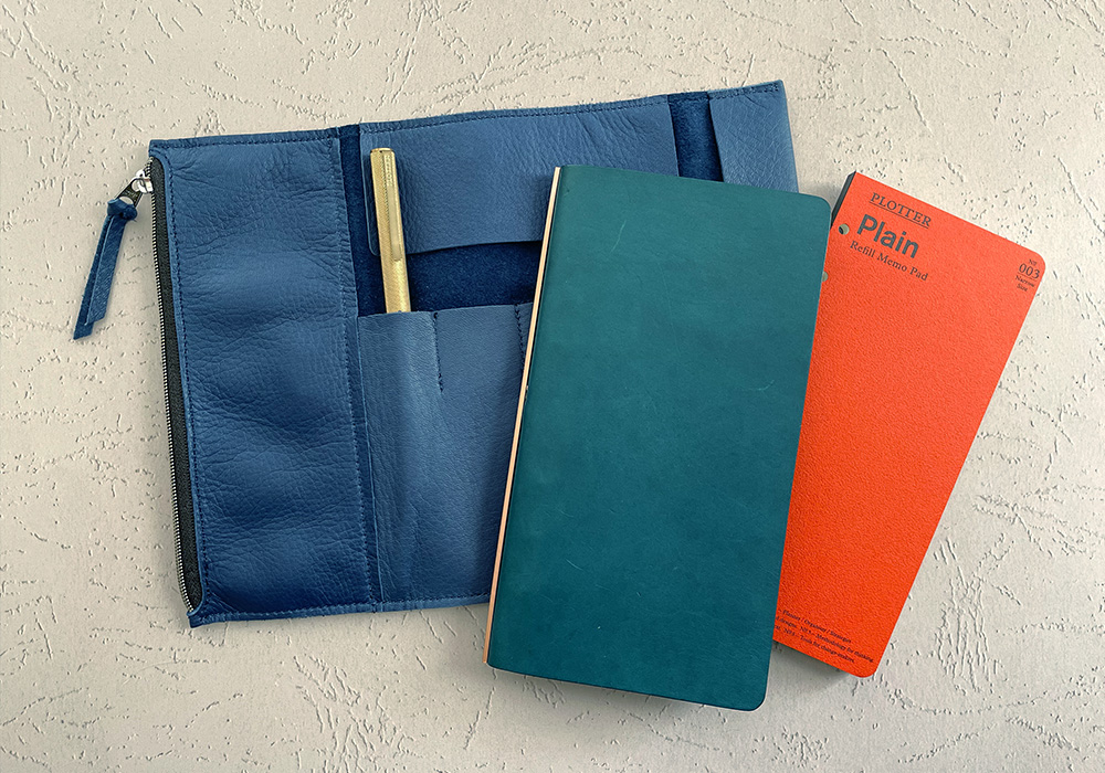 A PLOTTER Liscio Blue in Narrow Size next to a navy Roll Pen Case. 