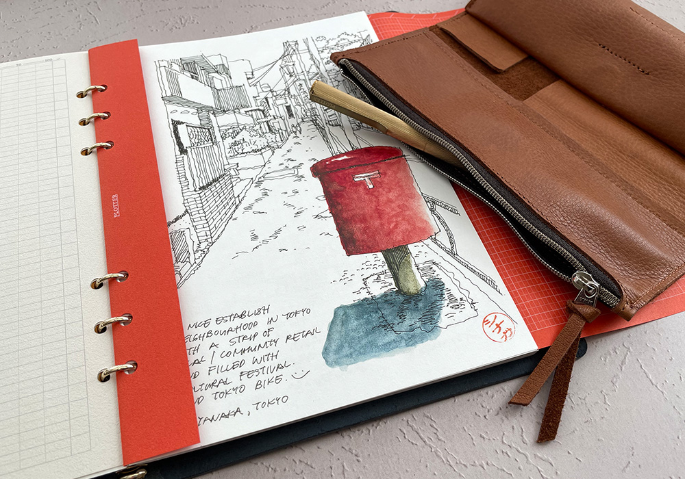 A brown Roll Pen Case next to an open spread of a PLOTTER with a drawing.