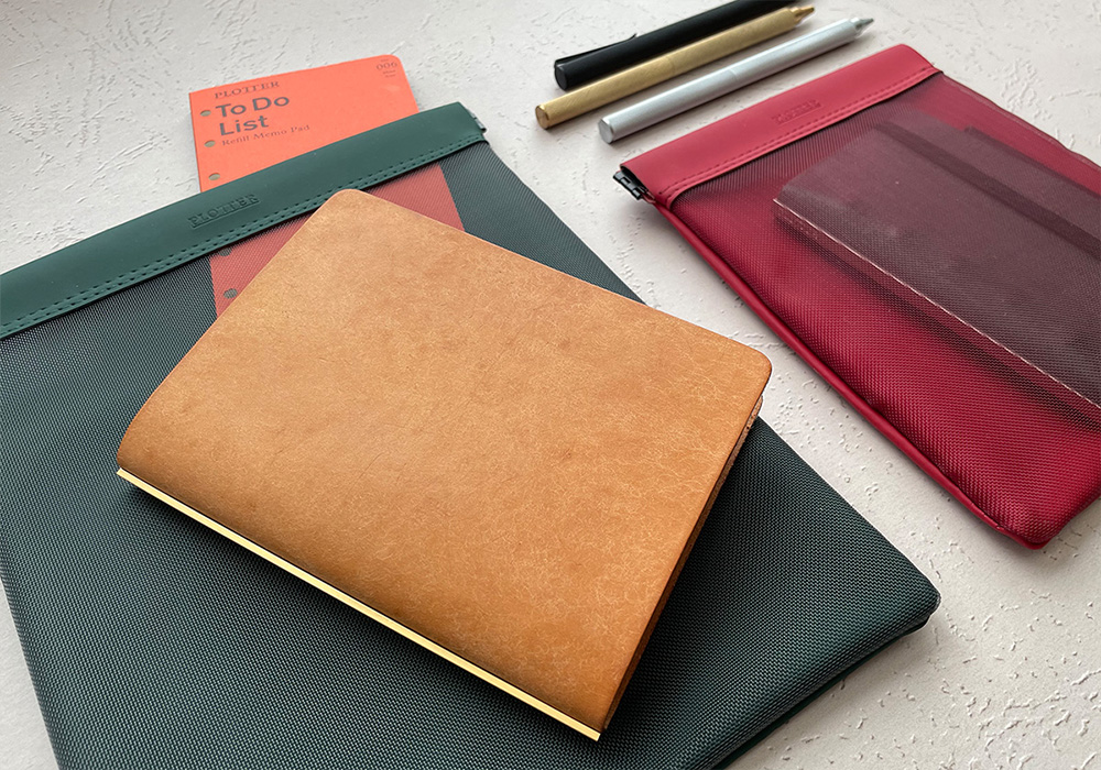 A PLOTTER Leather Binder Pueblo on top of a green Mesh Case next to other PLOTTER accessory and tools.