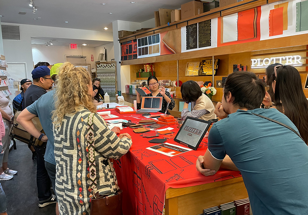 A group of customers gathered around a PLOTTER USA staff explaining the variety of PLOTTER Leather Binders.