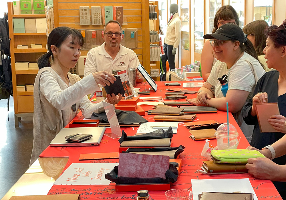 PLOTTER USA Staff explaining a PLOTTER Leather binder to customers across a table inside FLAX Pen to Paper.