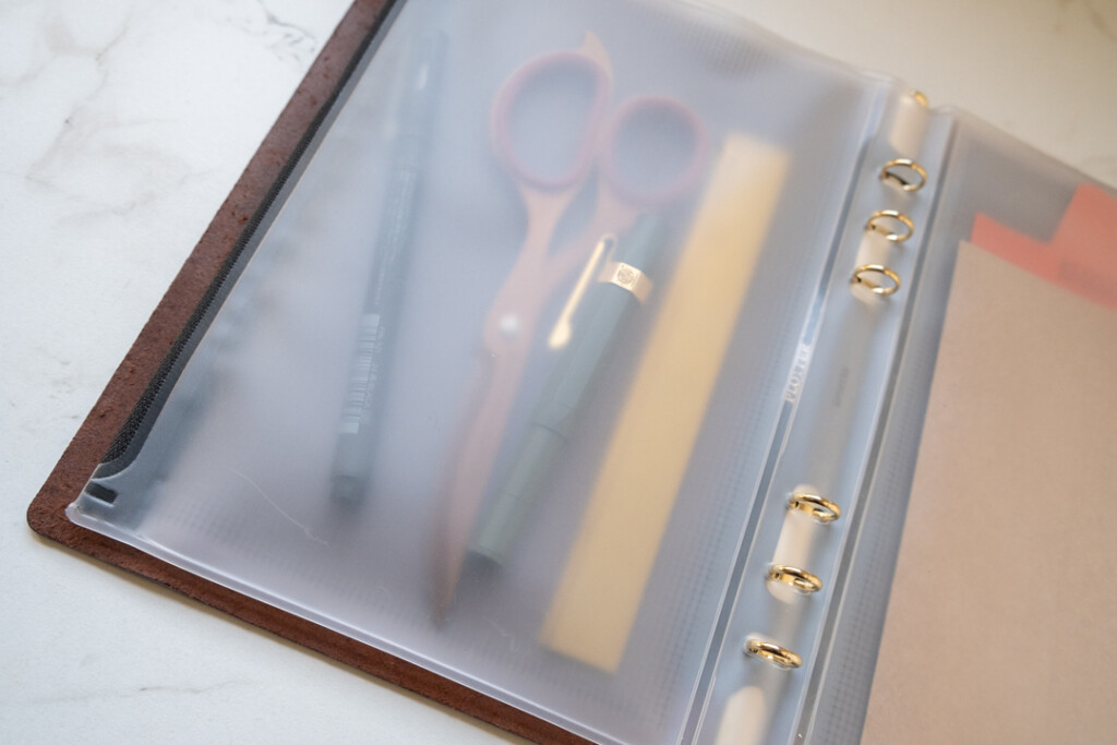 The interior side of a PLOTTER A5 Fastener Case holding a fountain pen, a drawing pen, a scissor, and a ruler.