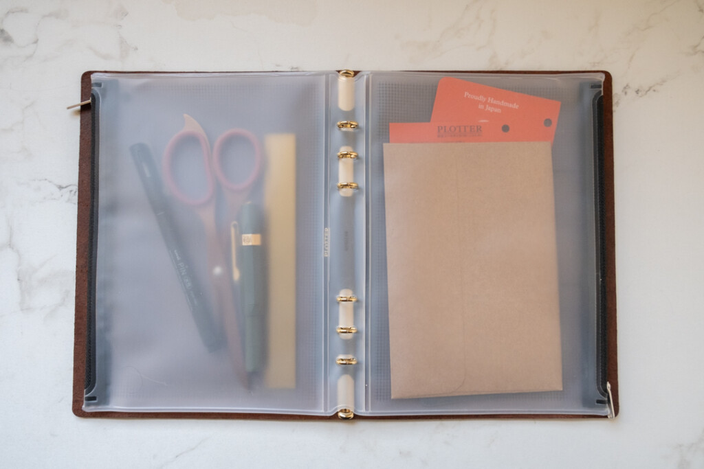 A PLOTTER Fastener Case in A5 Size inside a PLOTTER holding a variety of stationery tools.