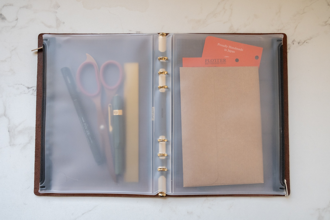 A PLOTTER Fastener Case in A5 Size inside a PLOTTER holding a variety of stationery tools.
