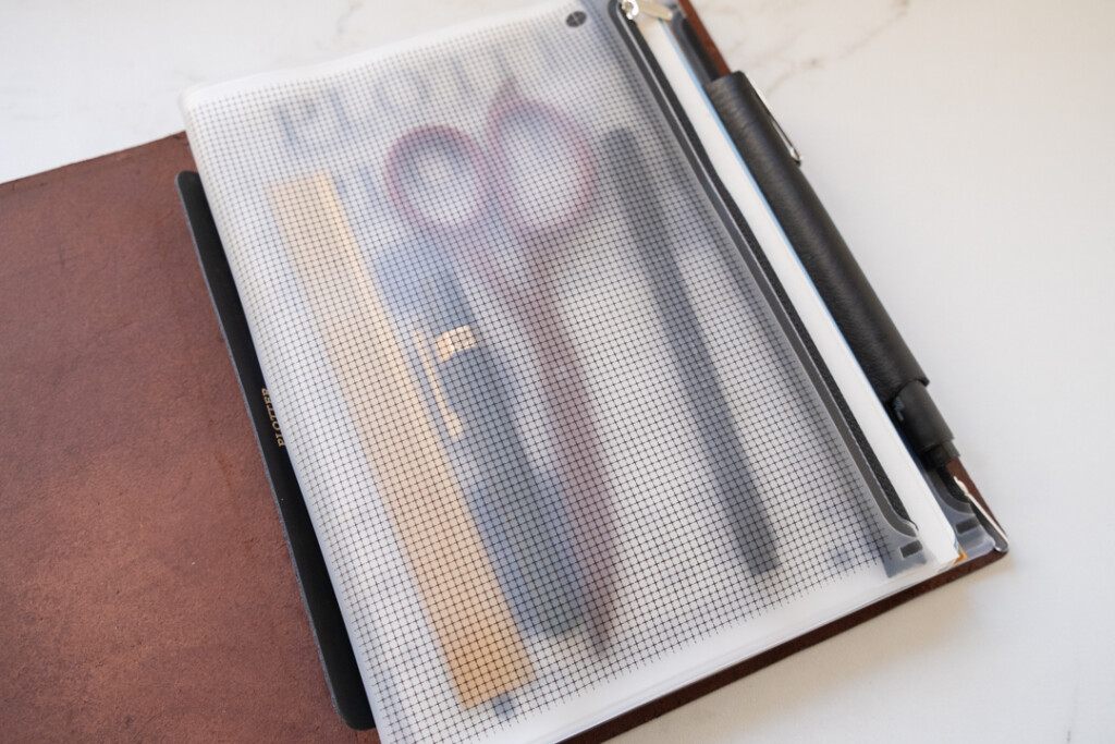 A PLOTTER Fastener Case in A5 Size holding a scissor, a fountain pen, a regular pen, and a ruler.