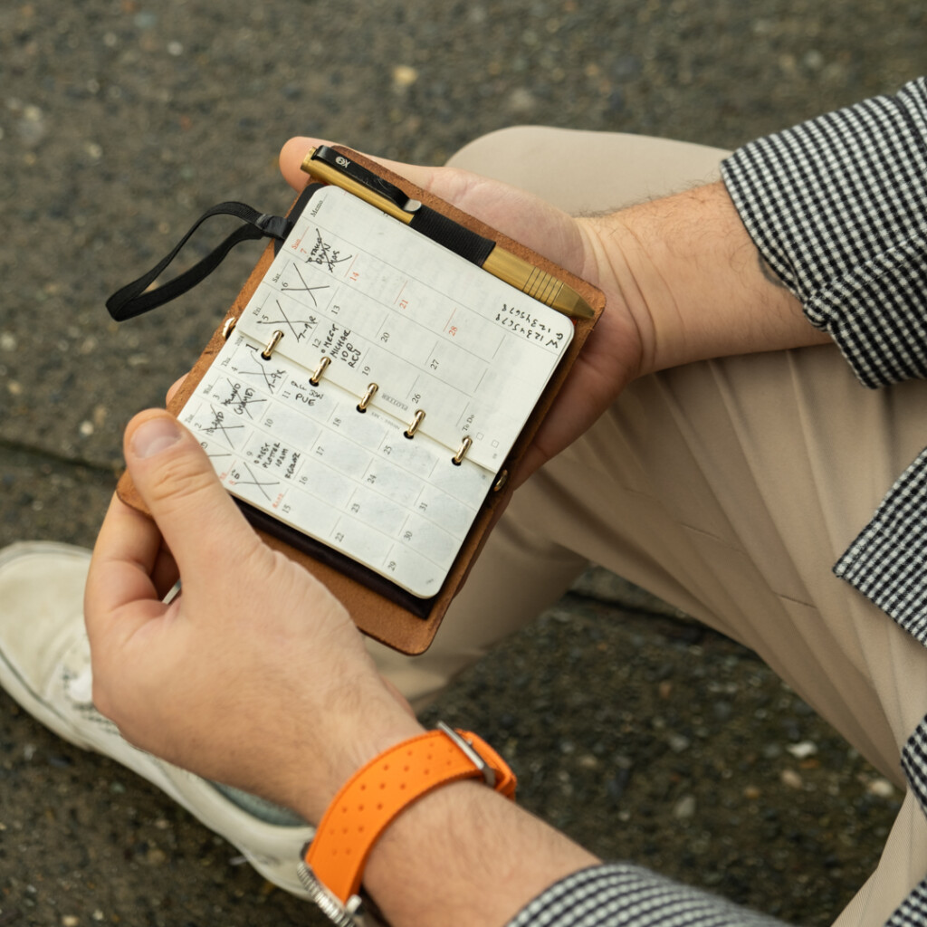 Chris Giannakos holding his open PLOTTER Mini 5 leather binder to a monthly calendar.