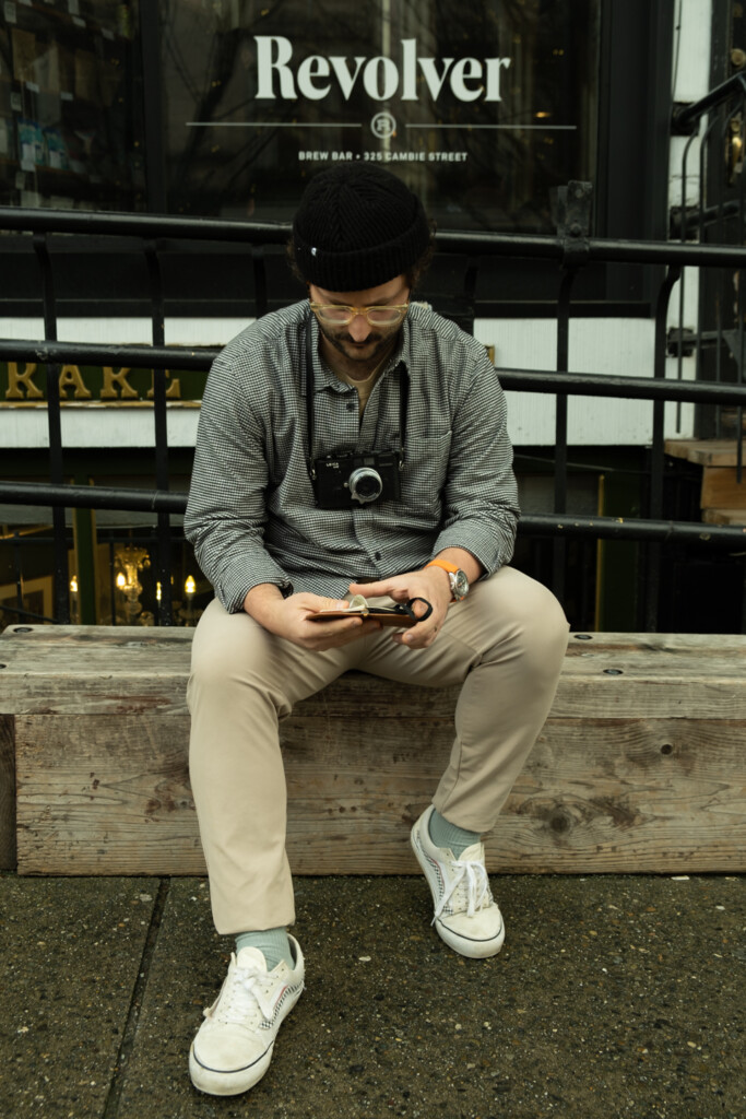 A portrait of Chris Giannakos holding his open PLOTTER Mini 5 leather binder in front of his coffee shop, Revolver Coffee.