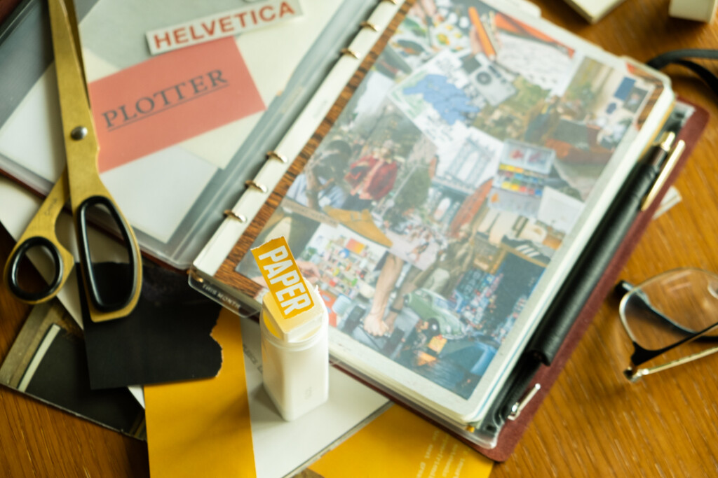 Collaging supplies and glue beside a collage vision board inside a PLOTTER Leather Binder.