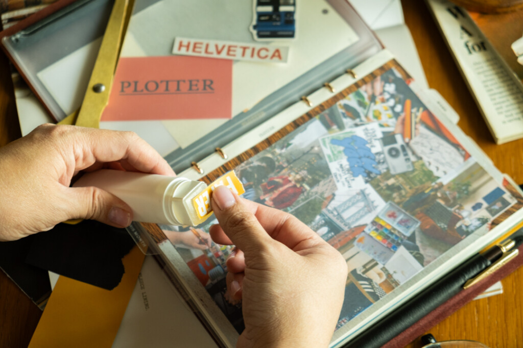 A person gluing an item to a collage vision board inside a PLOTTER Leather Binder.