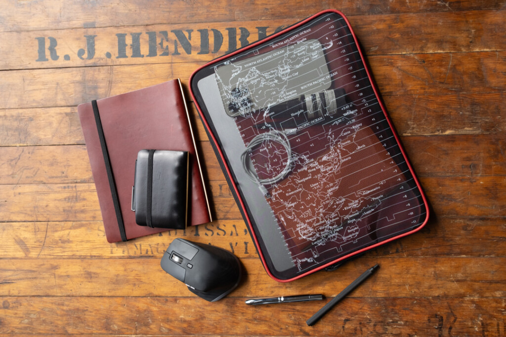 A PLOTTER A4 Mesh Zipper Case being used as a laptop case beside other tech devices and stationery.