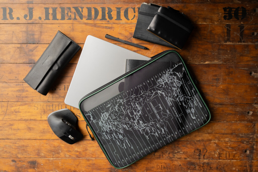 A PLOTTER A4 Mesh Zipper Case is being used as a laptop case beside other tech devices and stationery.