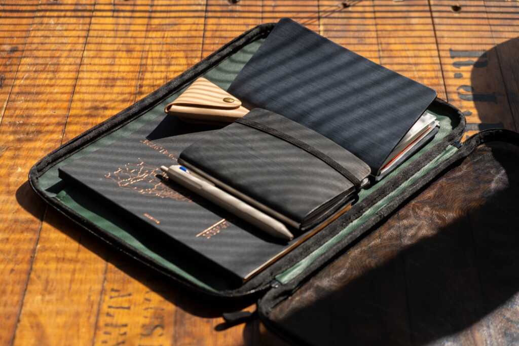 A PLOTTER A4 Mesh Zipper Case is open to show that it is being used as a laptop case filled with tech devices and stationery.