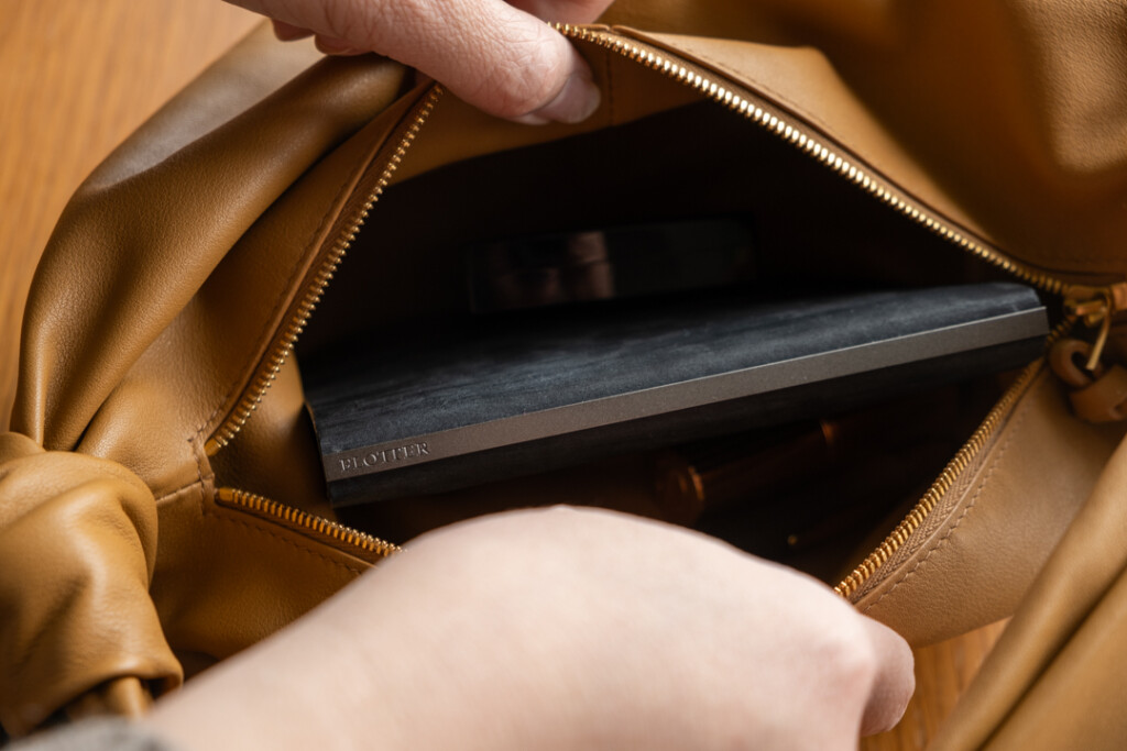 A person putting a PLOTTER Horse Hair II Mini Size Leather Binder in to a small tan purse.