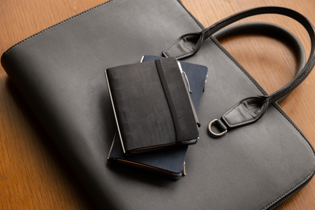 A PLOTTER Horse Hair II Narrow and Mini Size Leather Binder on top of a leather briefcase.
