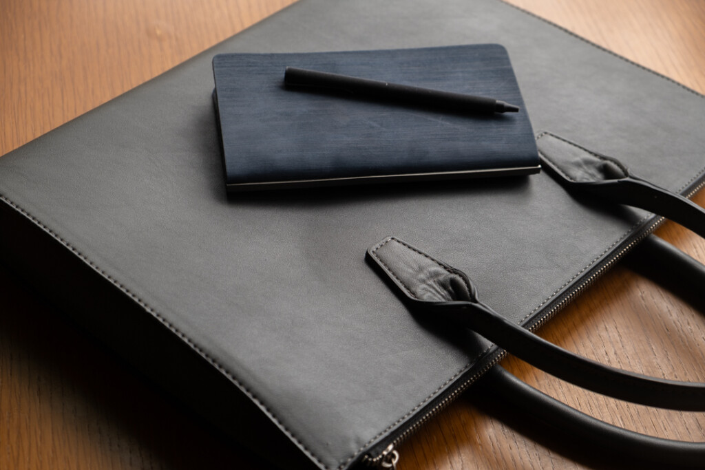 A PLOTTER Horse Hair II Narrow Size Leather Binder on top of a leather briefcase.