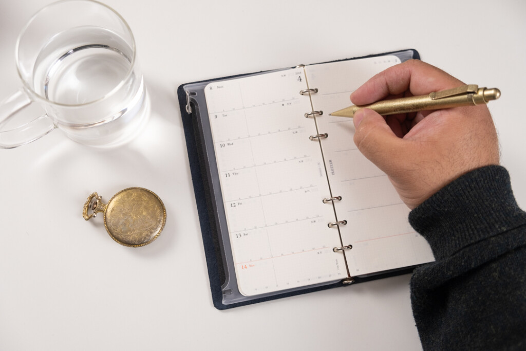 A person writing in a Narrow Size PLOTTER leather binder.