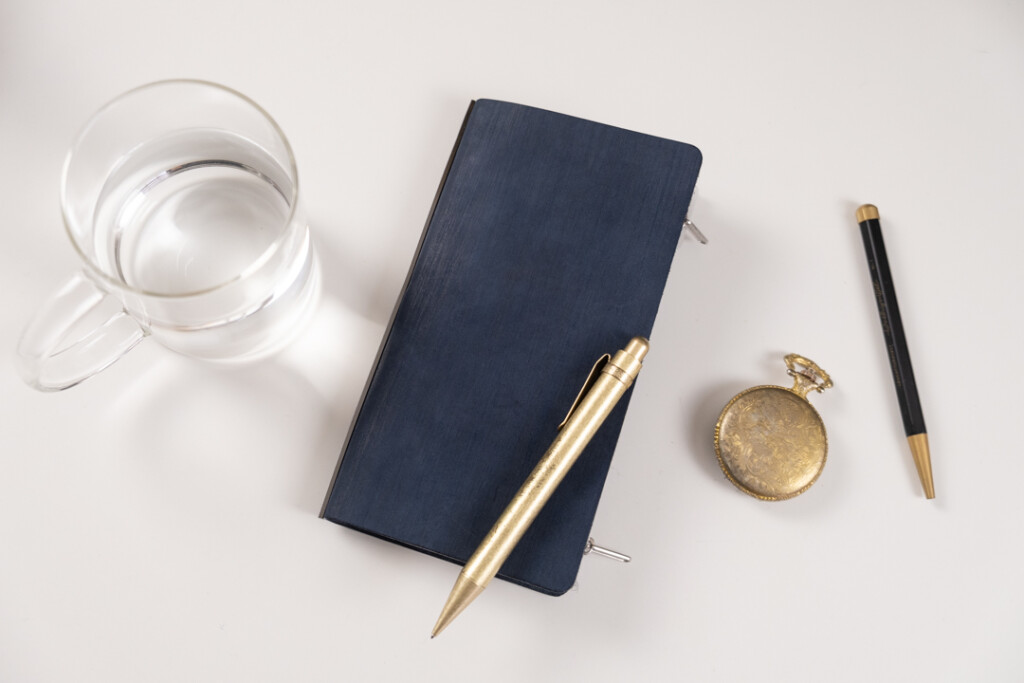 A PLOTTER Narrow Size in Horse Hair II Leather beside a cup of water and writing utensils. 
