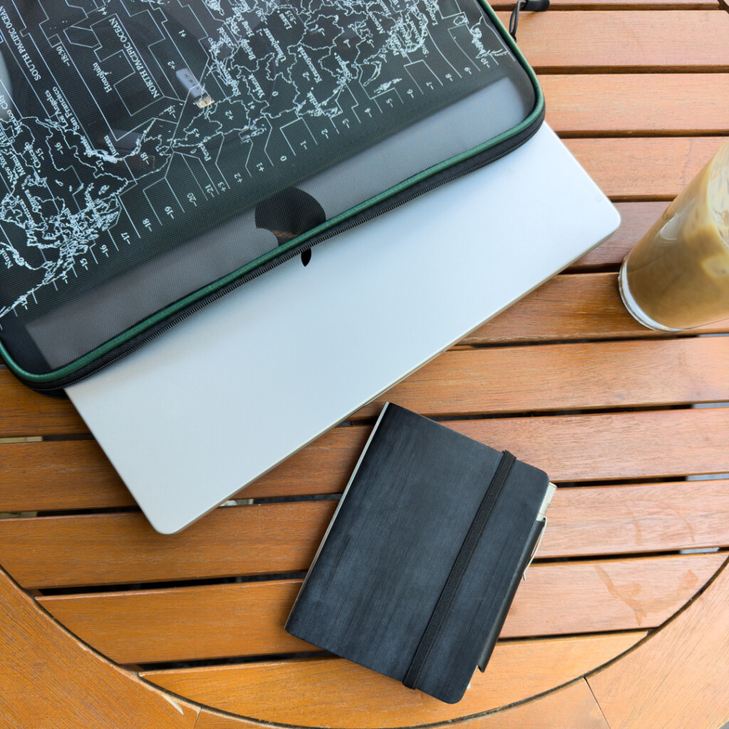A PLOTTER Mini Size in Horse Hair II Leather beside a laptop on a wooden table.