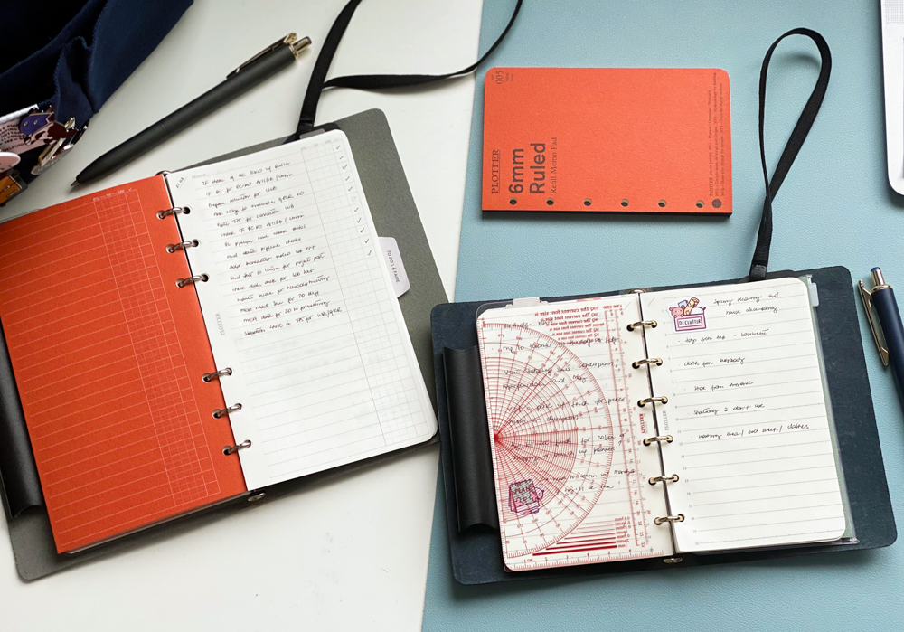Two PLOTTER leather binders on a desk both open to notes pages.