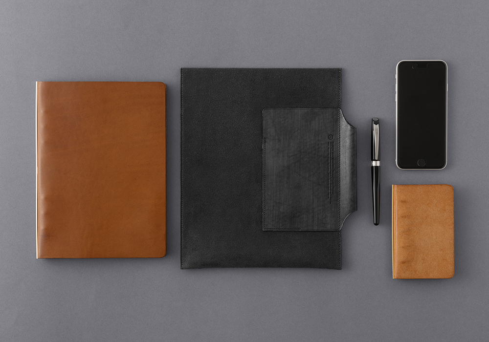 A pen, a mobile phone, a PLOTTER in Mini 5 Size, and a PLOTTER in A5 Size next to a Leather Binder Case