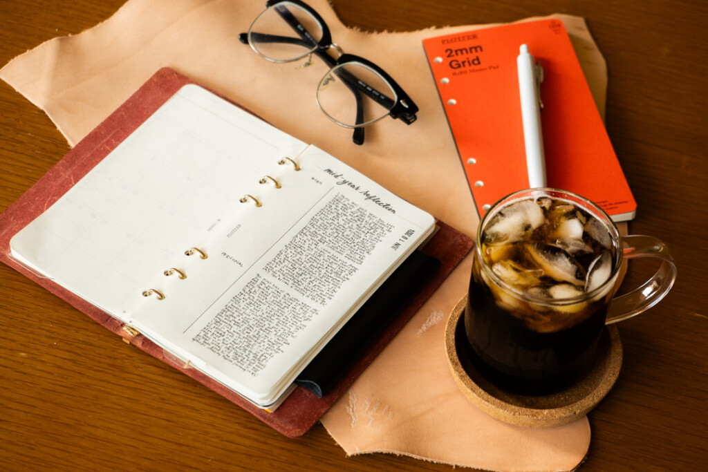 PLOTTER Leather Binder open with notes beside ice coffee, Refill Memo Pad, Pen and eye glasses.