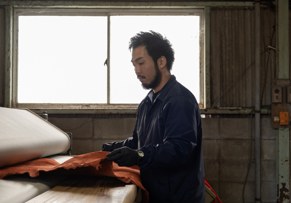 Leather craftsman holding orange leather that will be put into a leather press machine.