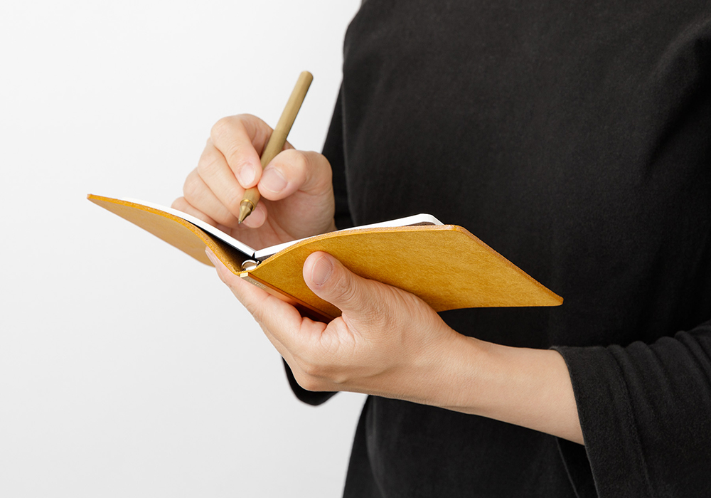 A person holding an opened Mini 5 Square leather binder and writing on it.