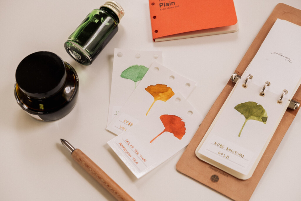 PLOTTER 3-Ring Leather Binder open to a green fountain pen ink swatch beside other ink swatches, ink bottles, refill memo pad, and ink swatching tool.