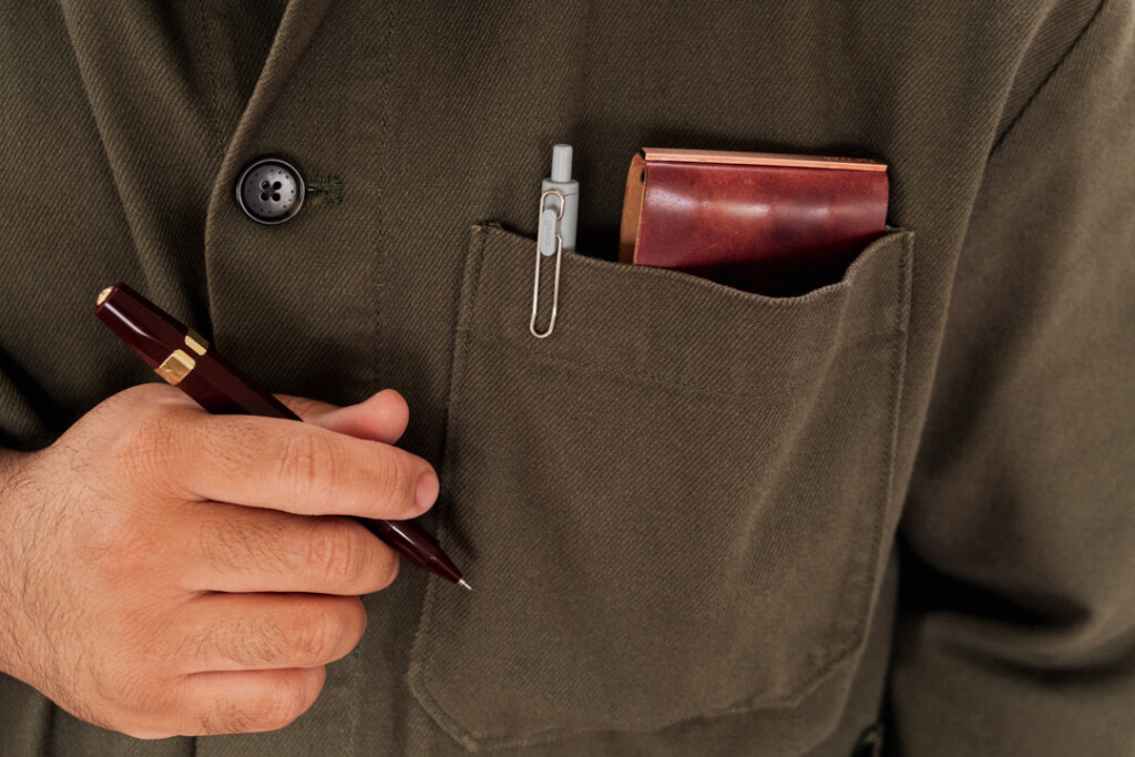 A person holding a pocket pen and a PLOTTER 3-Ring Leather Binder in their jacket pocket beside a pen.