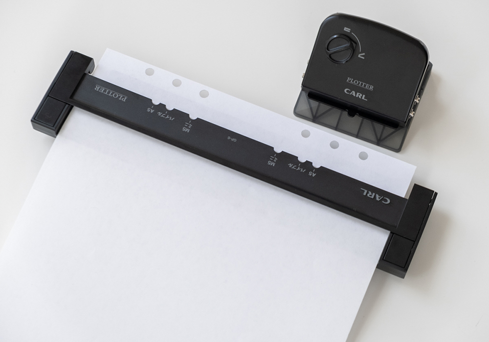 The Refill Maker Hole Punch demonstrating the two sets of holes that it can punch on a piece of paper.