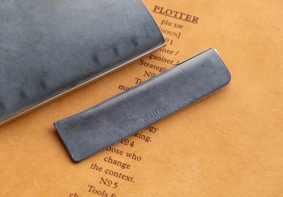 The PLOTTER Shiranami Leather Pen Sleeve beside a PLOTTER Leather Binder on top of a leather mat.