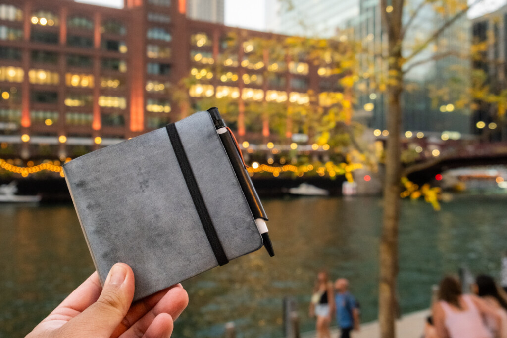 Person holding a PLOTTER Leather Binder in mini 5 square in front of the Chicago River Skyline.