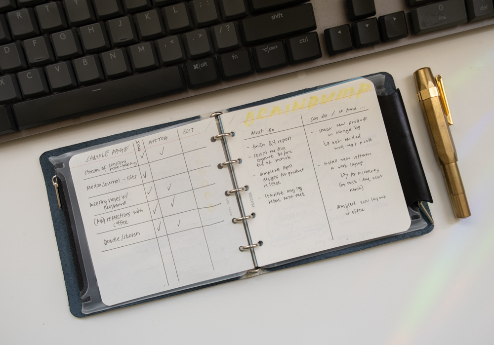 A PLOTTER Mini 5 Square Leather Binder and a fountain pen in front of a computer keyboard, with notes inside the binder.