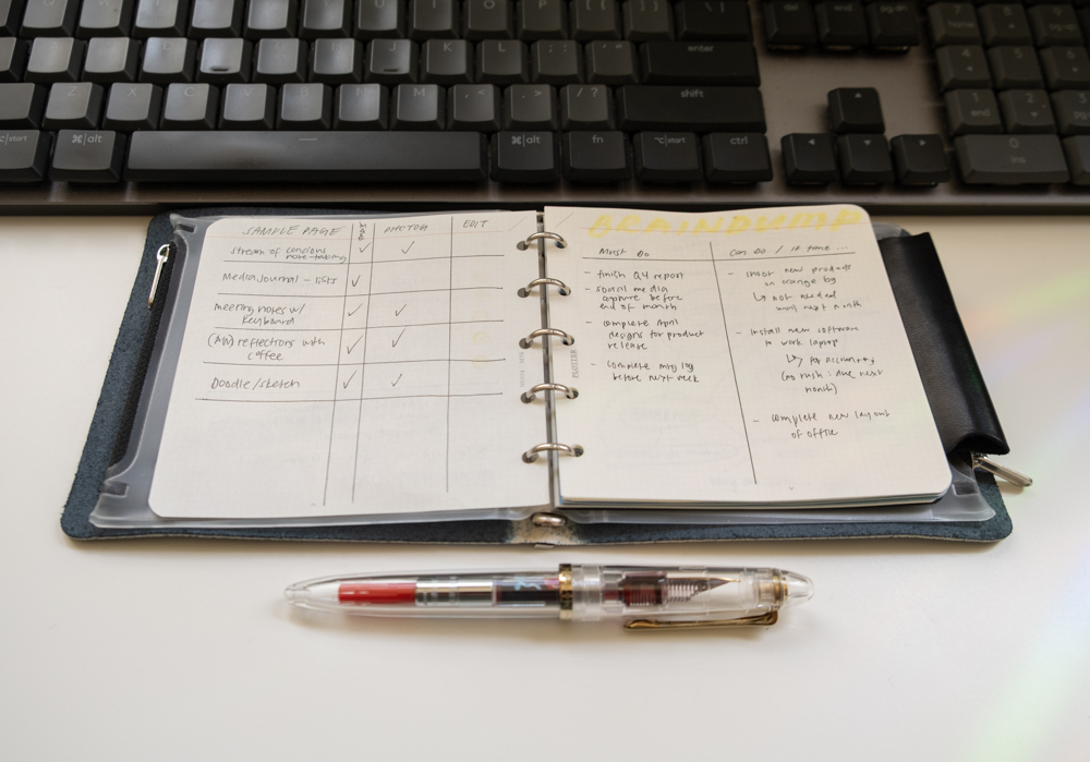 A PLOTTER Mini 5 Square Leather Binder and a fountain pen in front of a computer keyboard, with notes inside the binder.