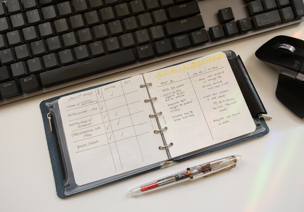 A PLOTTER Mini 5 Square Leather Binder and a fountain pen in front of a computer keyboard, with notes inside the binder.