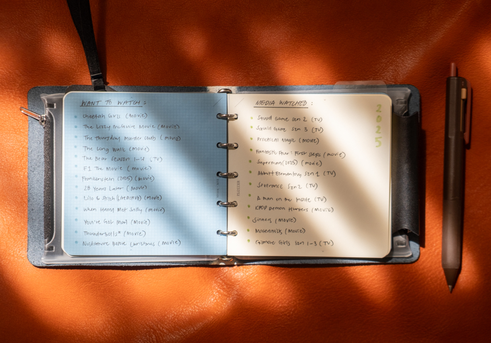 TV and Movie notes and watchlist inside a PLOTTER Mini 5 Square Size Leather Binder on an orange leather background in high-contrast lighting.