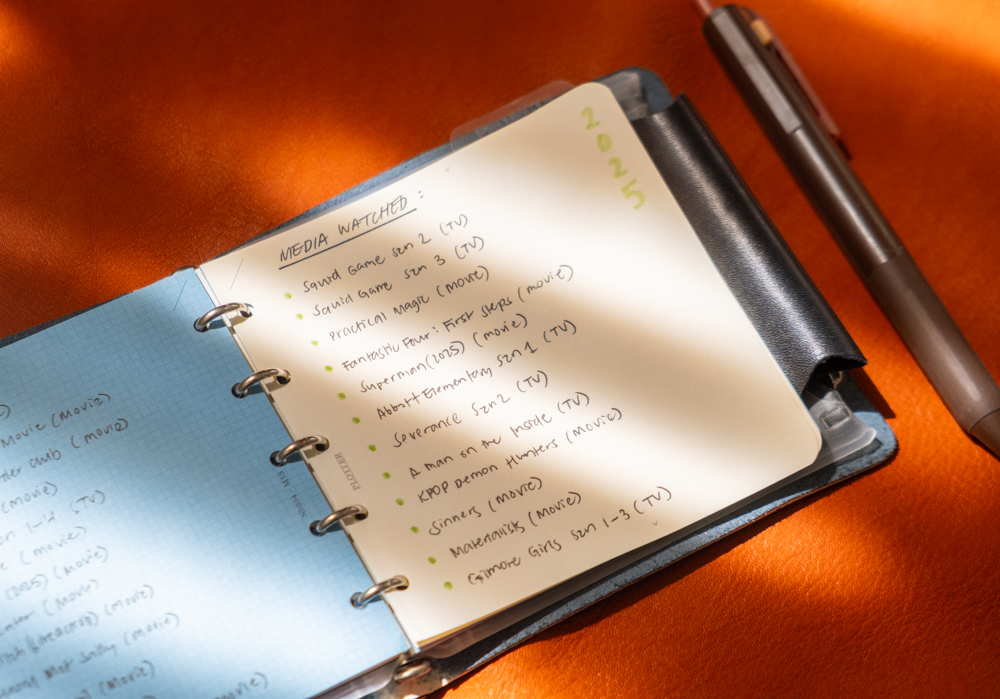 TV and Movie notes and watchlist inside a PLOTTER Mini 5 Square Size Leather Binder on an orange leather background in high-contrast lighting.