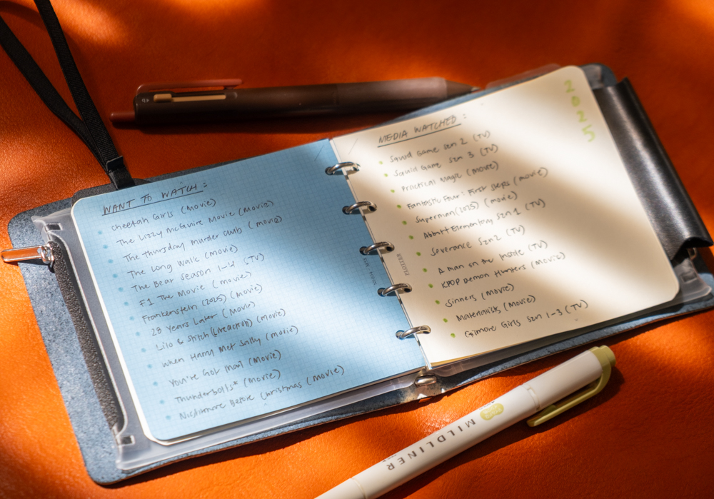 TV and Movie notes and watchlist inside a PLOTTER Mini 5 Square Size Leather Binder on an orange leather background in high-contrast lighting.