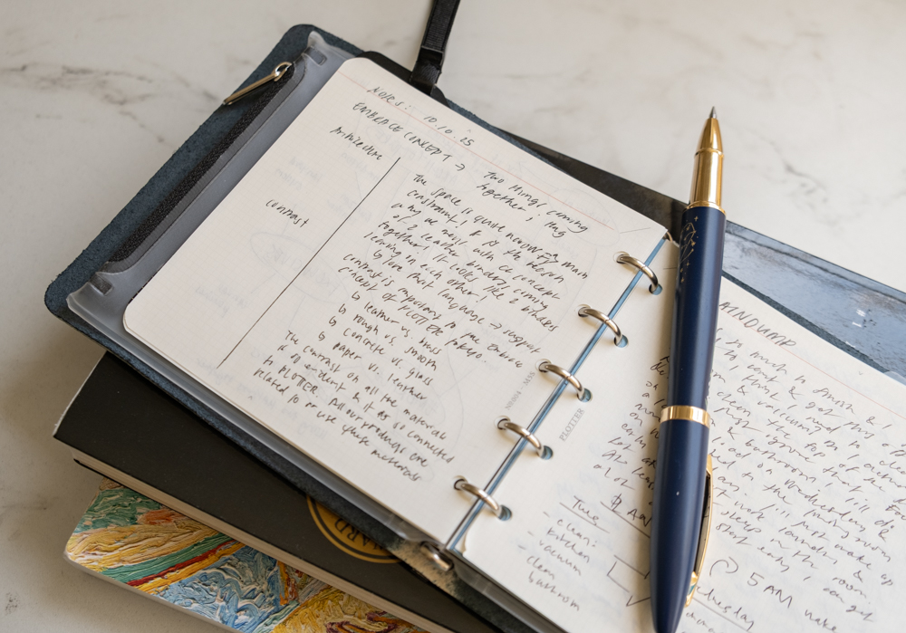 Stream of consciousness notes and journal reflections inside a PLOTTER Mini 5 Square Size Leather Binder beside a pen and books.
