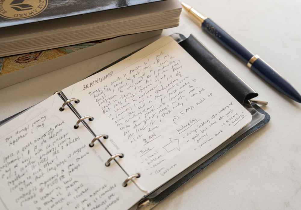 Stream of consciousness notes and journal reflections inside a PLOTTER Mini 5 Square Size Leather Binder beside a pen and books.