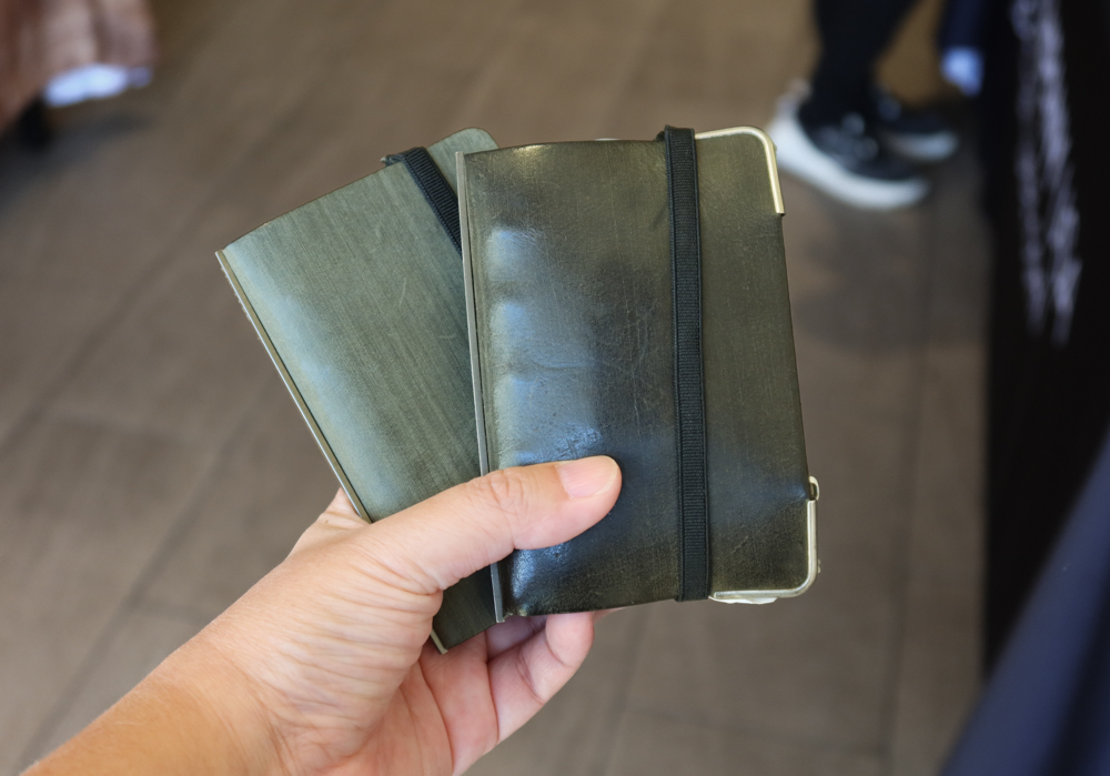 A person holding two PLOTTER Horse Hair II Leather Binders in Green Mini 5 Size but one is new and one is older and has a heavy patina on it.