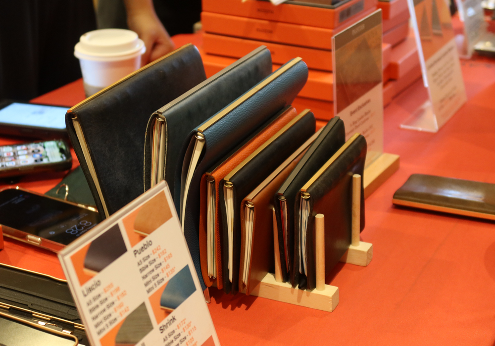 Sample PLOTTER Leather Binders on a wooden rack at the PLOTTER USA table at the SF Pen Show.