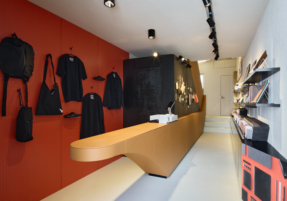 The first floor features a table wrapped entirely in leather, against an orange wall with lifestyle apparel and accessories.