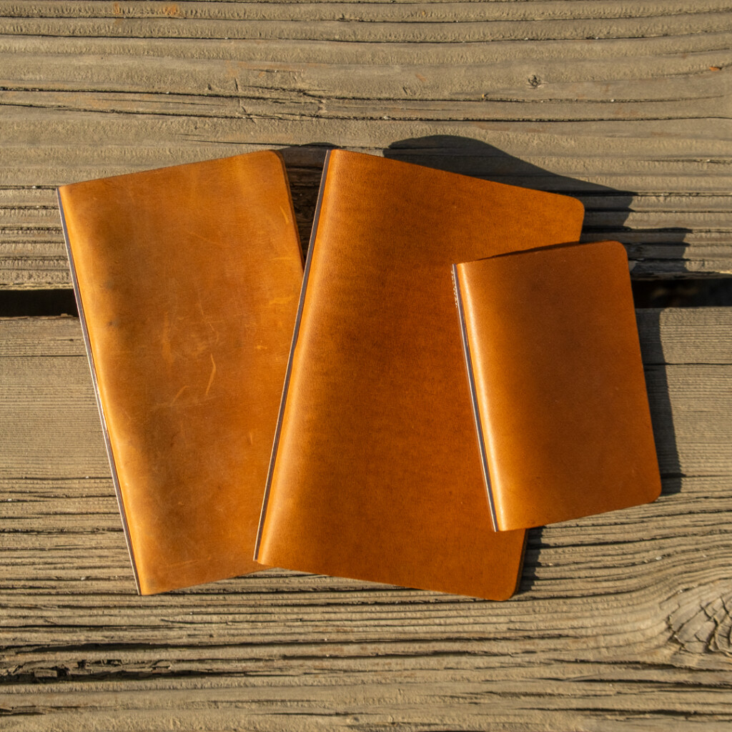 Three PLOTTER Leather Binders in Horween Predator Leather in Narrow Size, Bible Size and Mini 5 Size. All three binders are resting on a weathered wooden table.